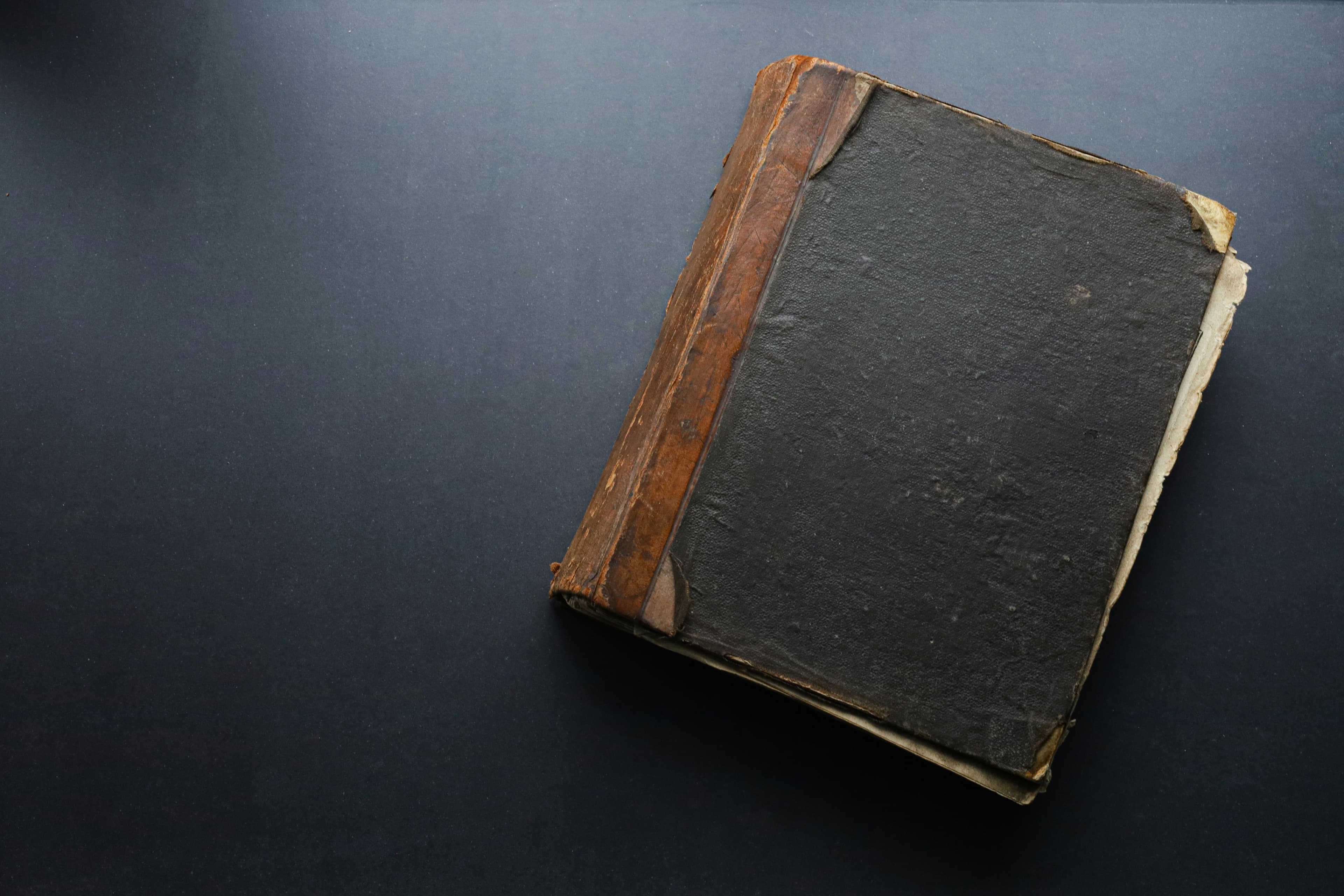 Photographie d'un vieux carnet relié en cuir usé, posé sur un fond sombre.