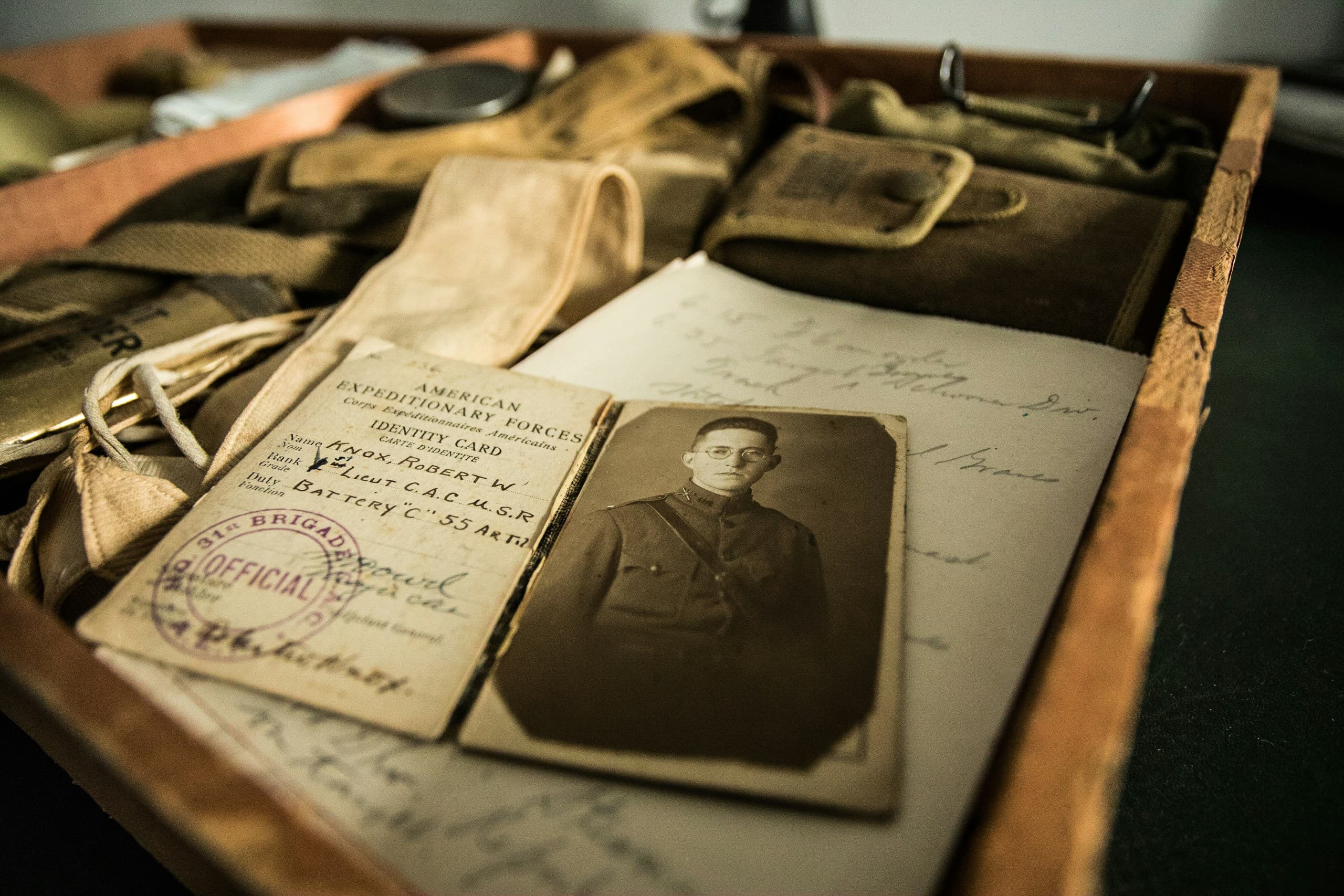 Photographie ancienne d'une carte d'identité militaire avec le portrait d'un jeune homme, parmi des effets personnels d'époque.